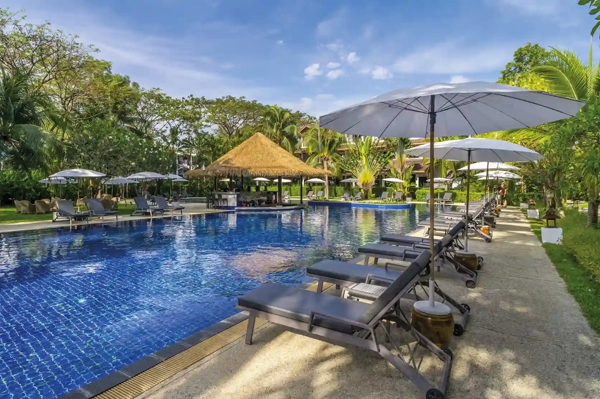 Grosszuegige Poolanlage mit Liegen und Sonnenschirmen in tropischer Gartenlandschaft