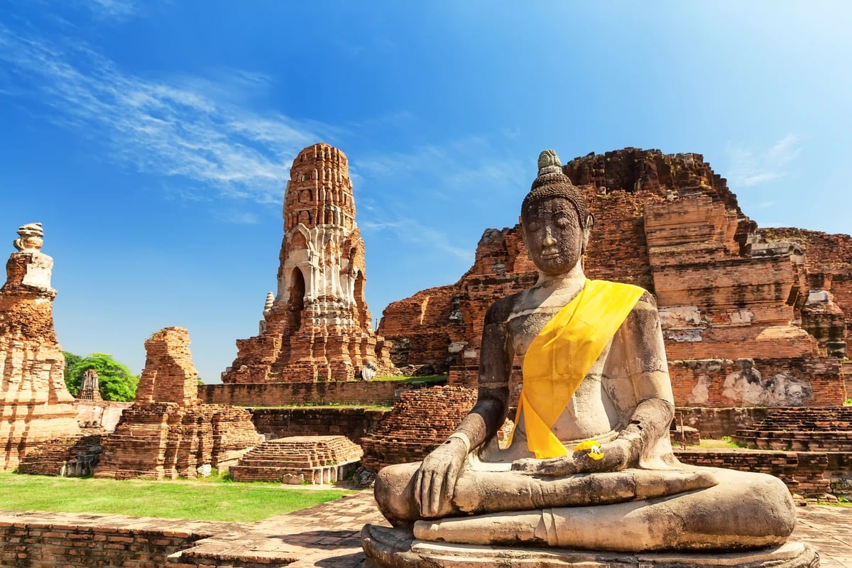 Historische Buddha Statue mit gelbem Tuch vor Tempelruinen in Ayutthaya