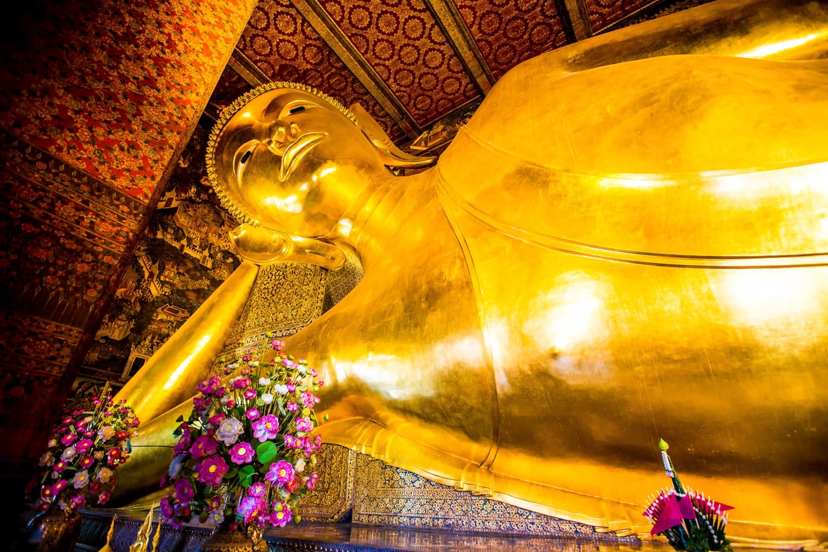 Vergoldete liegende Buddha Statue im Inneren eines Tempels mit Blumenopfern und reich verzierten Wänden