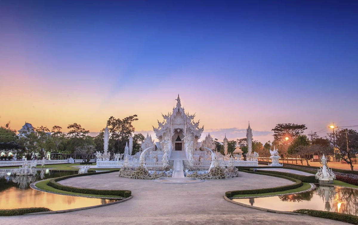 Weisser Tempel Wat Rong Khun bei Sonnenuntergang mit spiegelnden Wasserbecken und filigranen Skulpturen