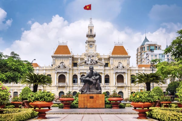 Historisches Gebäude in Ho Chi Minh City mit Statue, Palmen und vietnamesischer Flagge