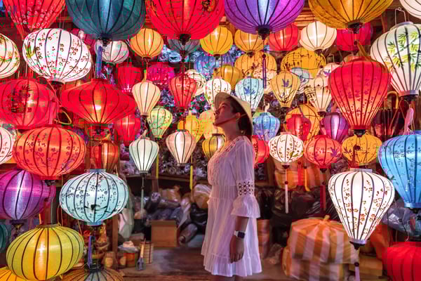Frau steht zwischen farbenfrohen Laternen in einer Gasse von Hoi An bei Nacht