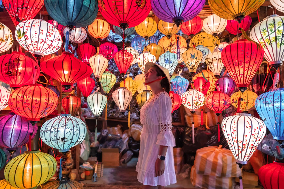 Frau steht zwischen farbenfrohen Laternen in einer Gasse von Hoi An bei Nacht