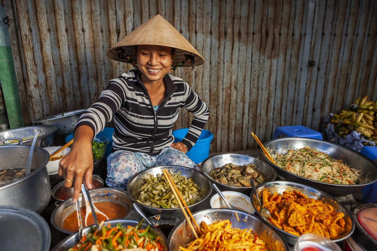 Strassenverkäuferin bereitet vietnamesische Speisen an mehreren Schüsseln zu