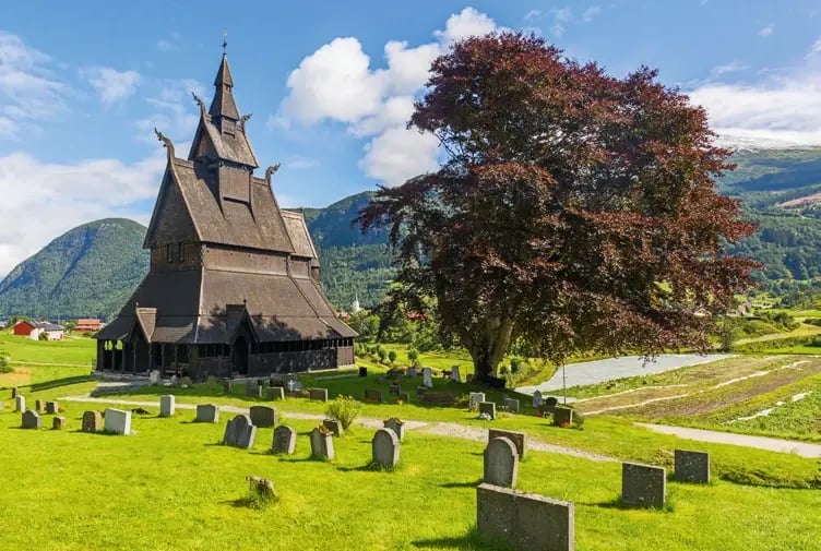 Historische Hopperstad-Stabkirche mit Friedhof inmitten einer grünen Fjordlandschaft.