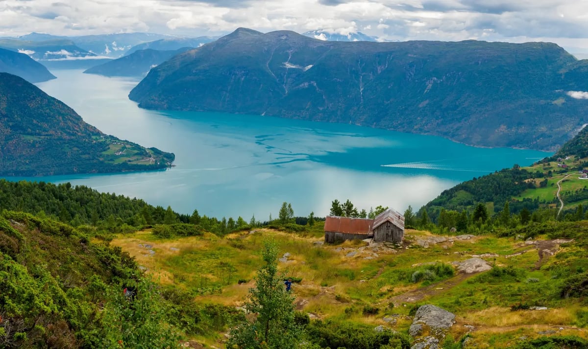 Panoramablick über den Lustrafjord mit Bergen, grünen Hängen und einer Berghütte.