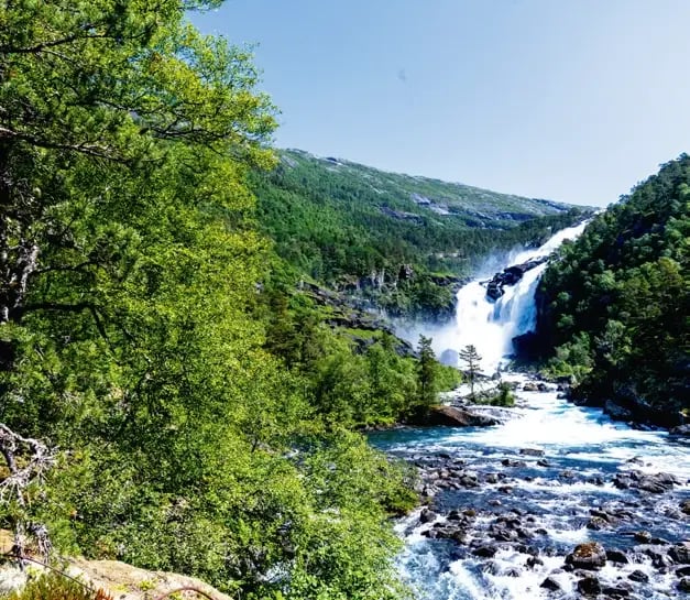 Nystafossen-Wasserfall inmitten dichter Wälder und einer felsigen Flusslandschaft.