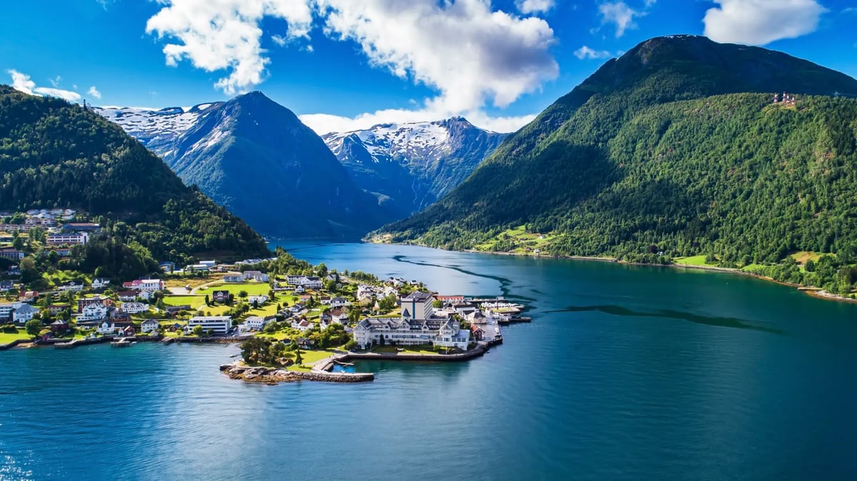Blick über den Sognefjord mit idyllischem Fjorddorf und schneebedeckten Bergen.