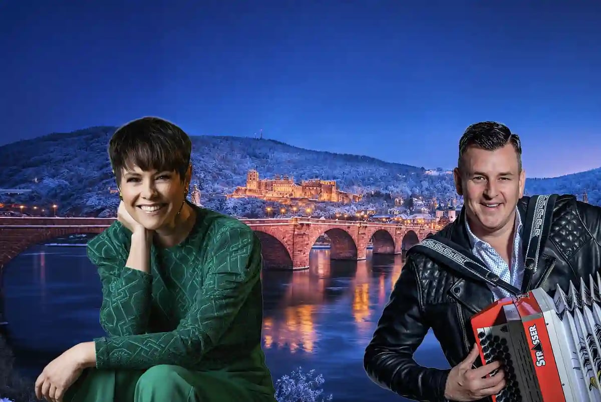 Eine lächelnde Frau im grünen Kleid und ein Mann in schwarzer Lederjacke mit einem Akkordeon, hineingezogen vor dem nächtlichen Panorama der Alten Brücke und des Schlosses in Heidelberg.