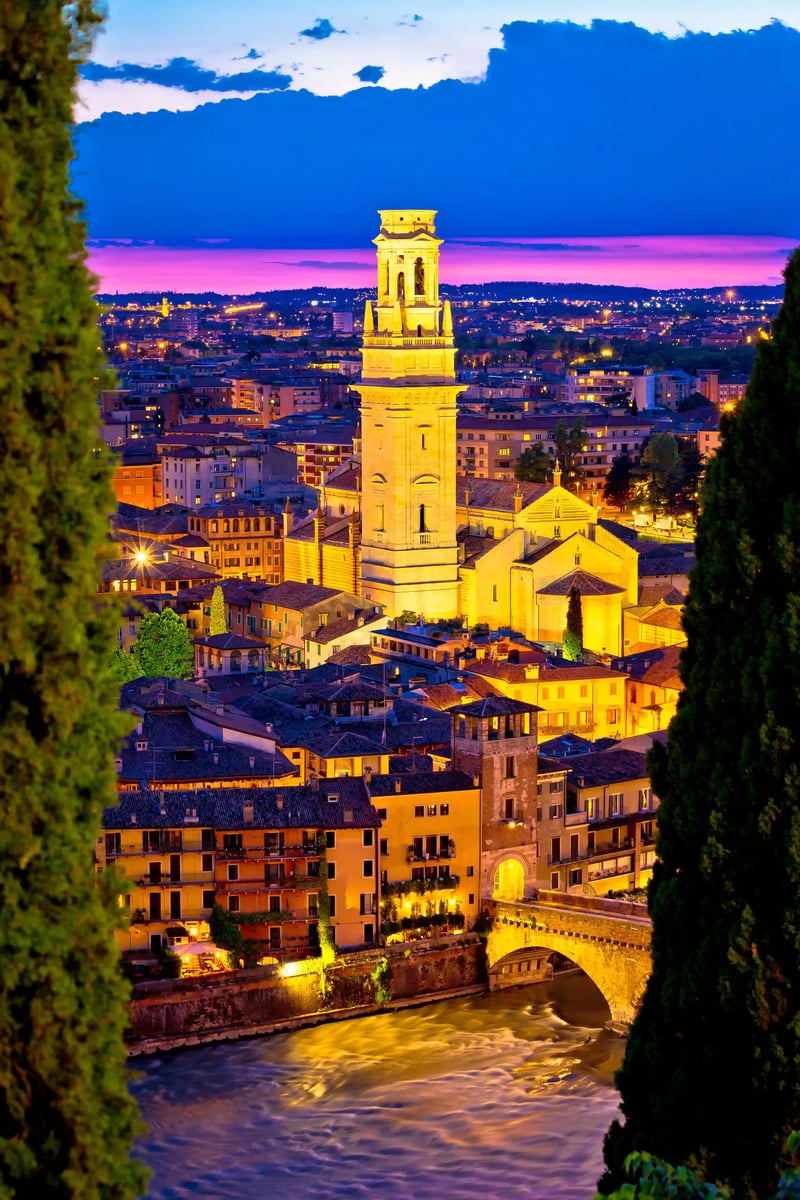 Blick auf Verona bei Abenddämmerung mit beleuchtetem Kirchturm und Fluss