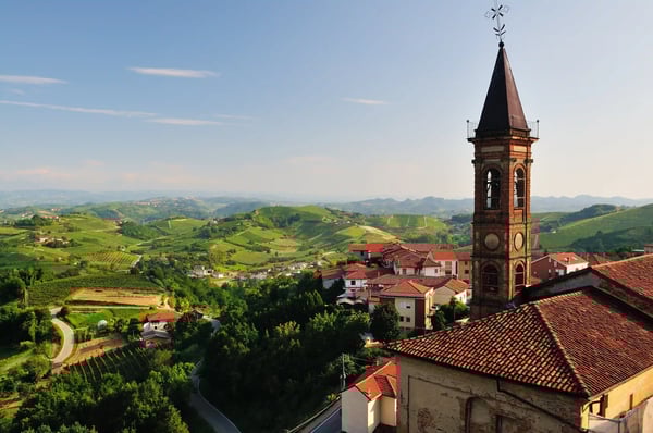 Kirchturm eines Dorfes mit Blick auf grüne Weinberge und Hügel im Piemont