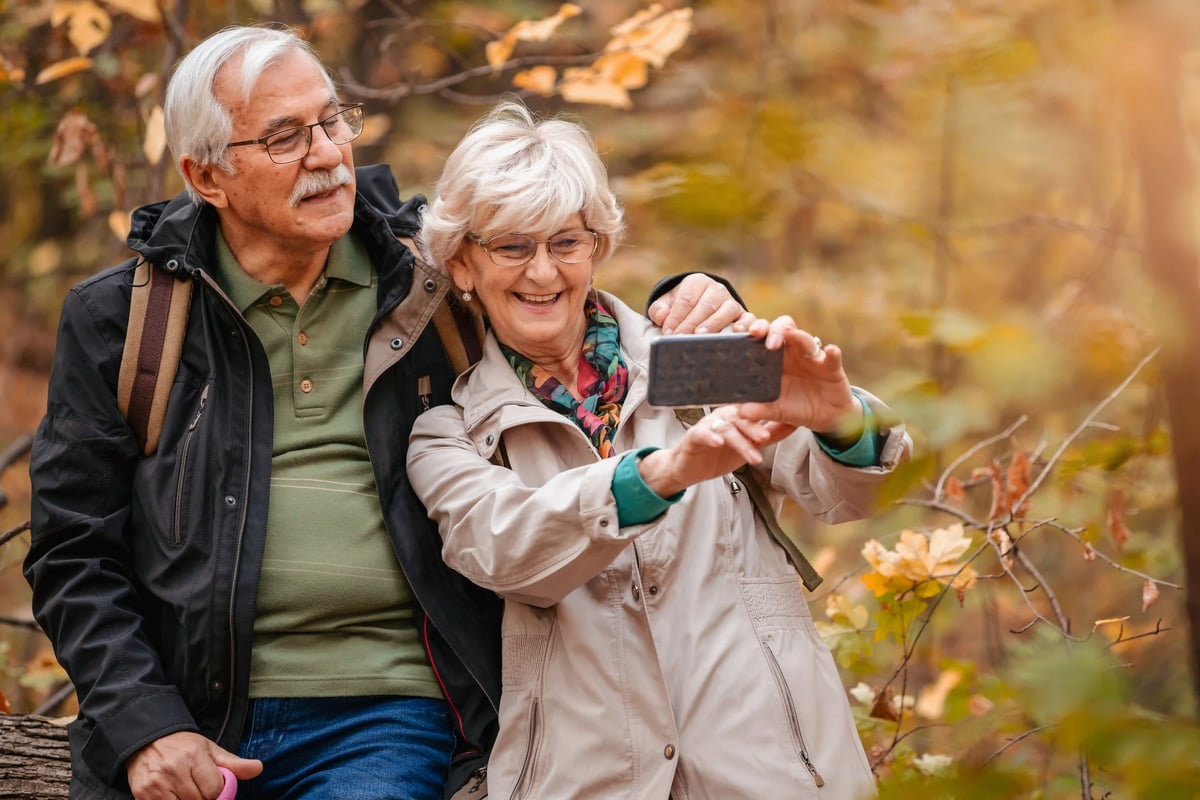 Couple senior prenant une photo avec un smartphone lors d’une promenade en forêt automnale