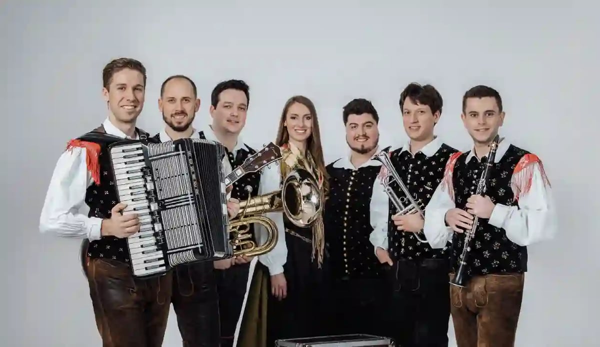 Musikgruppe in traditioneller Tracht mit Akkordeon Blechbläsern und Klarinette vor hellem Hintergrund