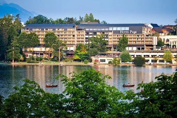 Hotel Park am Ufer des Bleder Sees mit Ruderbooten auf dem Wasser und Bäumen im Vordergrund