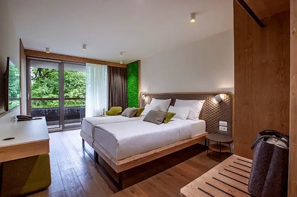 Modern eingerichtetes Hotelzimmer mit Doppelbett Holzfussboden Sitzbank und Balkon mit Blick ins Grüne