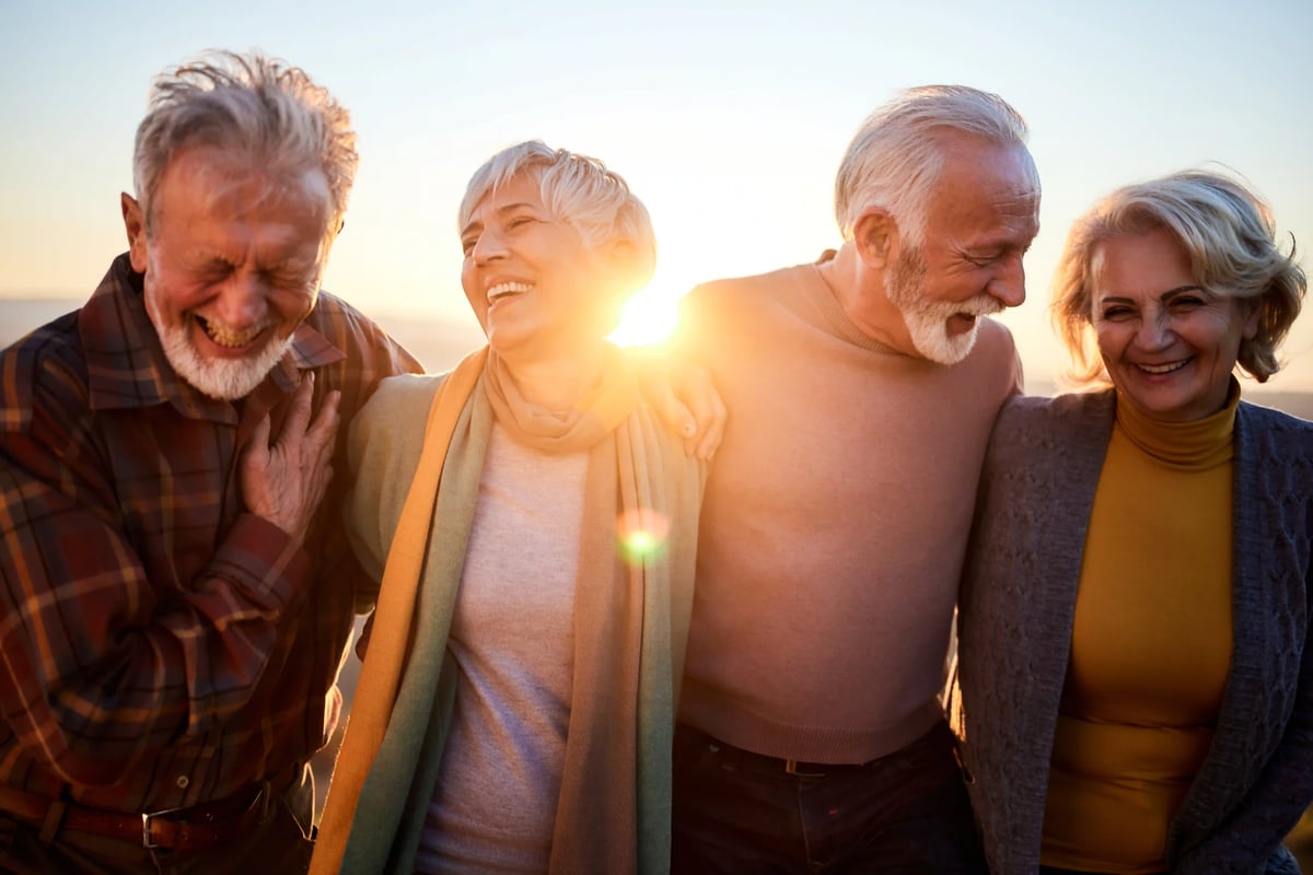 Vier ältere Menschen lachen gemeinsam bei Sonnenuntergang