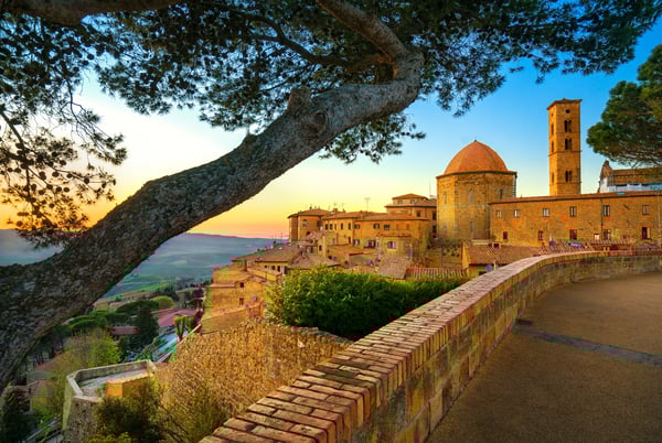 Blick auf die historische Altstadt von Volterra mit Stadtmauer, Kuppelbau und weiter Hügellandschaft im Abendlicht