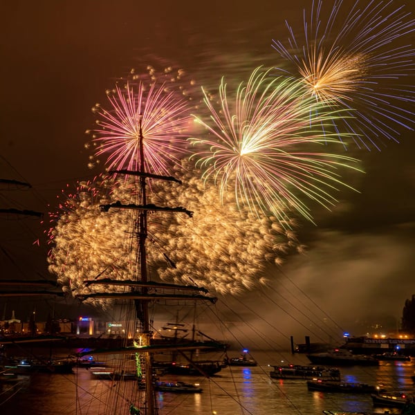Buntes Feuerwerk über dem Hamburger Hafen bei Nacht mit beleuchteten Schiffen und Masten im Vordergrund