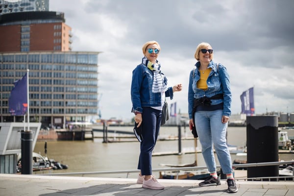Zwei Frauen spazieren lachend an der Hamburger Hafenpromenade mit moderner Architektur im Hintergrund