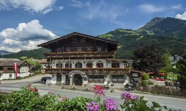 Traditionelles Tiroler Hotel mit Holzfassade, Balkonen und Berglandschaft im Hintergrund