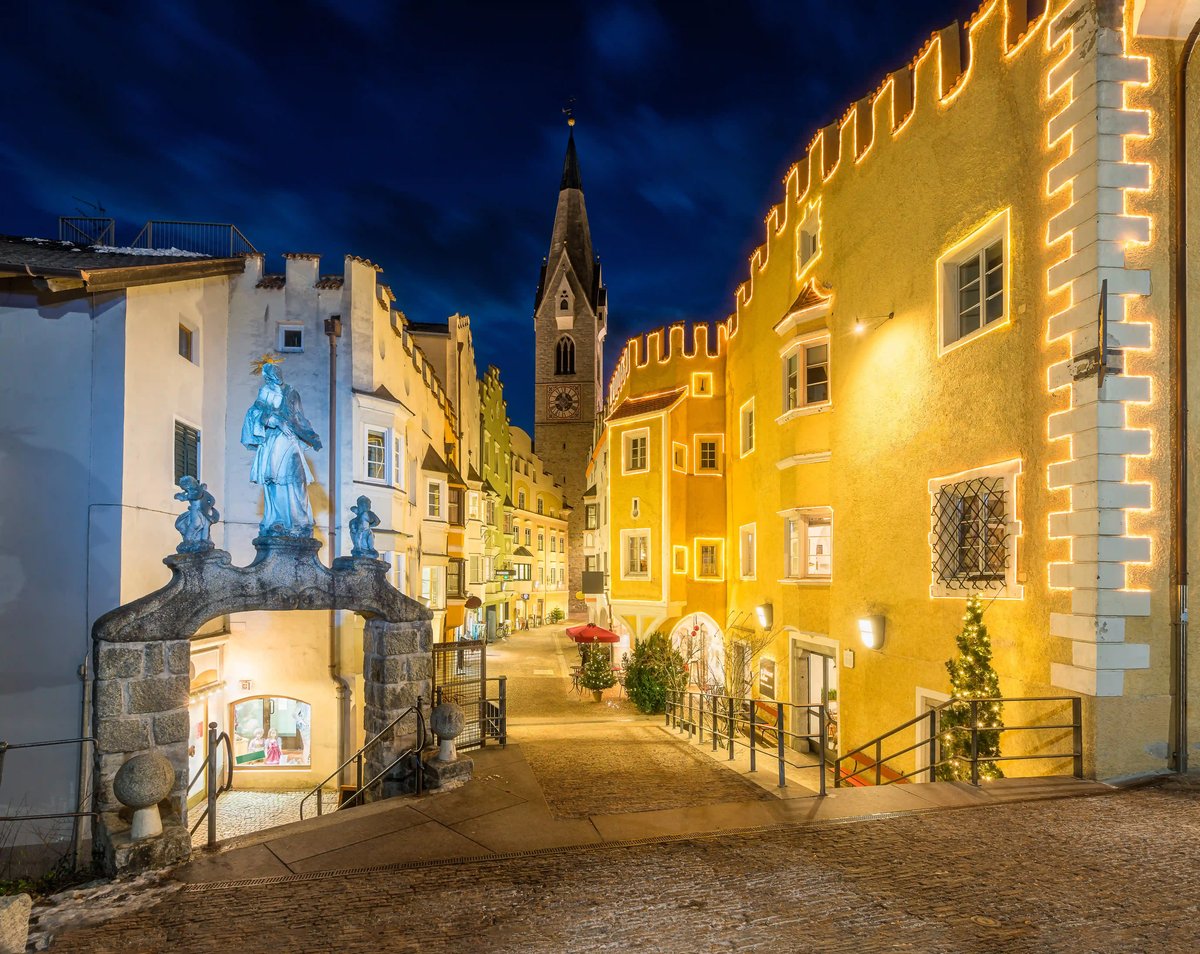Historische Altstadt von Brixen mit festlich beleuchteten Gassen und Kirchturm bei Nacht.