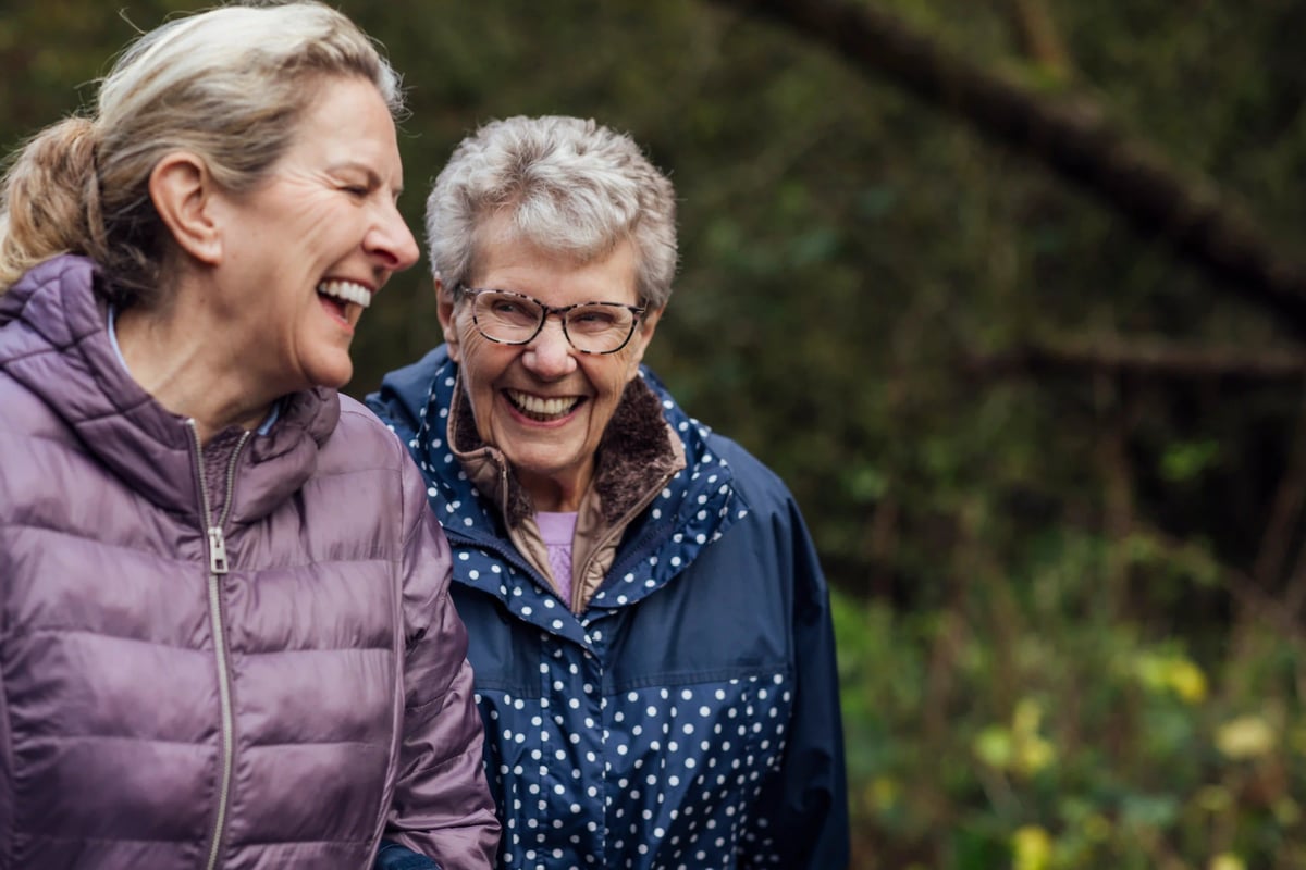 Zwei ältere Frauen lachen gemeinsam bei einem Spaziergang in der Natur
