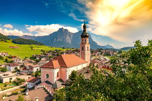 Blick auf Kastelruth mit Kirchturm, Dorfhäusern und Dolomiten im Hintergrund