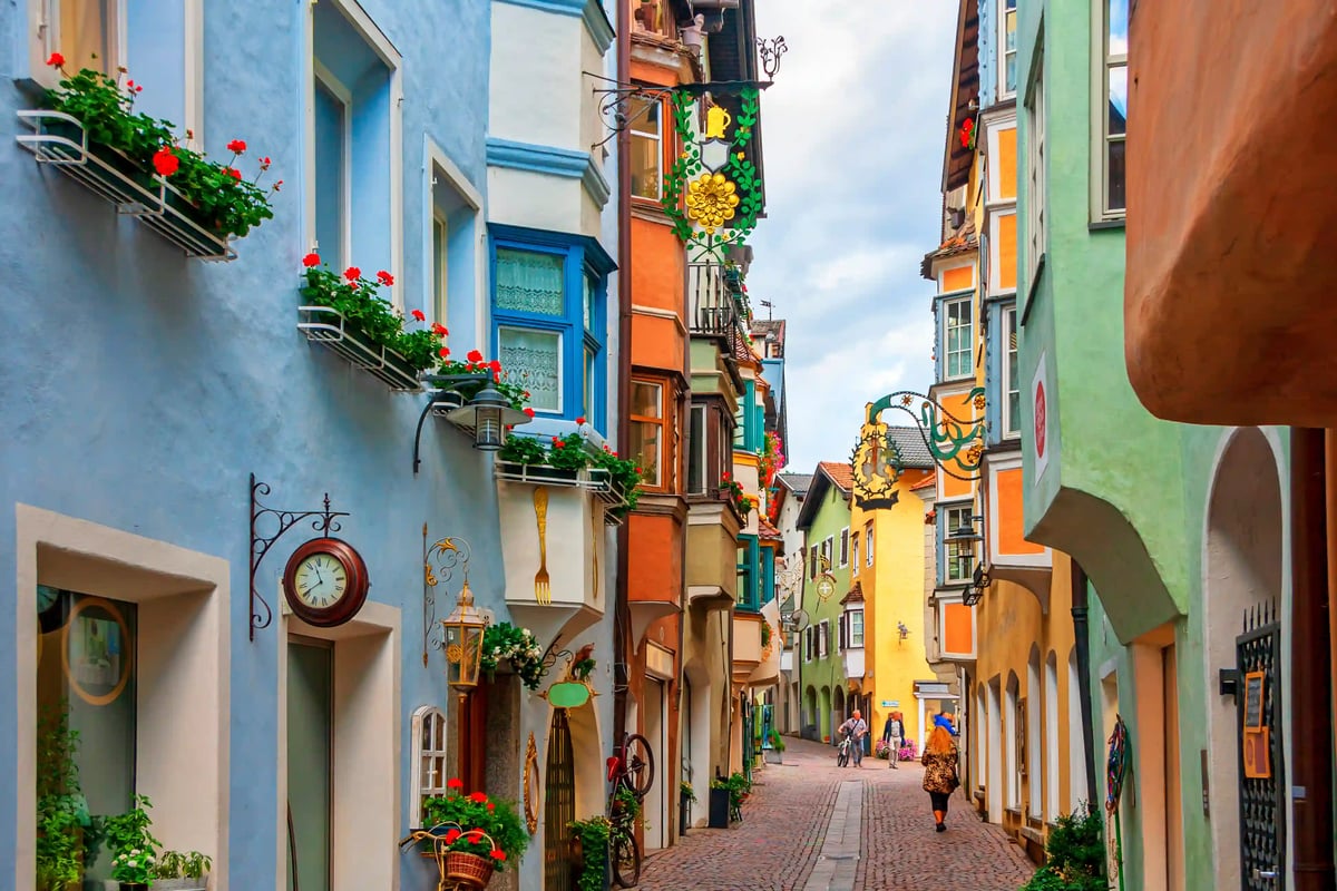 Schmale Altstadtgasse mit bunten Häuserfassaden, Blumen und schmiedeeisernen Schildern