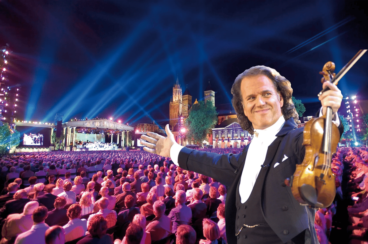 Chef dorchestre tenant un violon salue un large public devant une scène en plein air illuminée de nuit