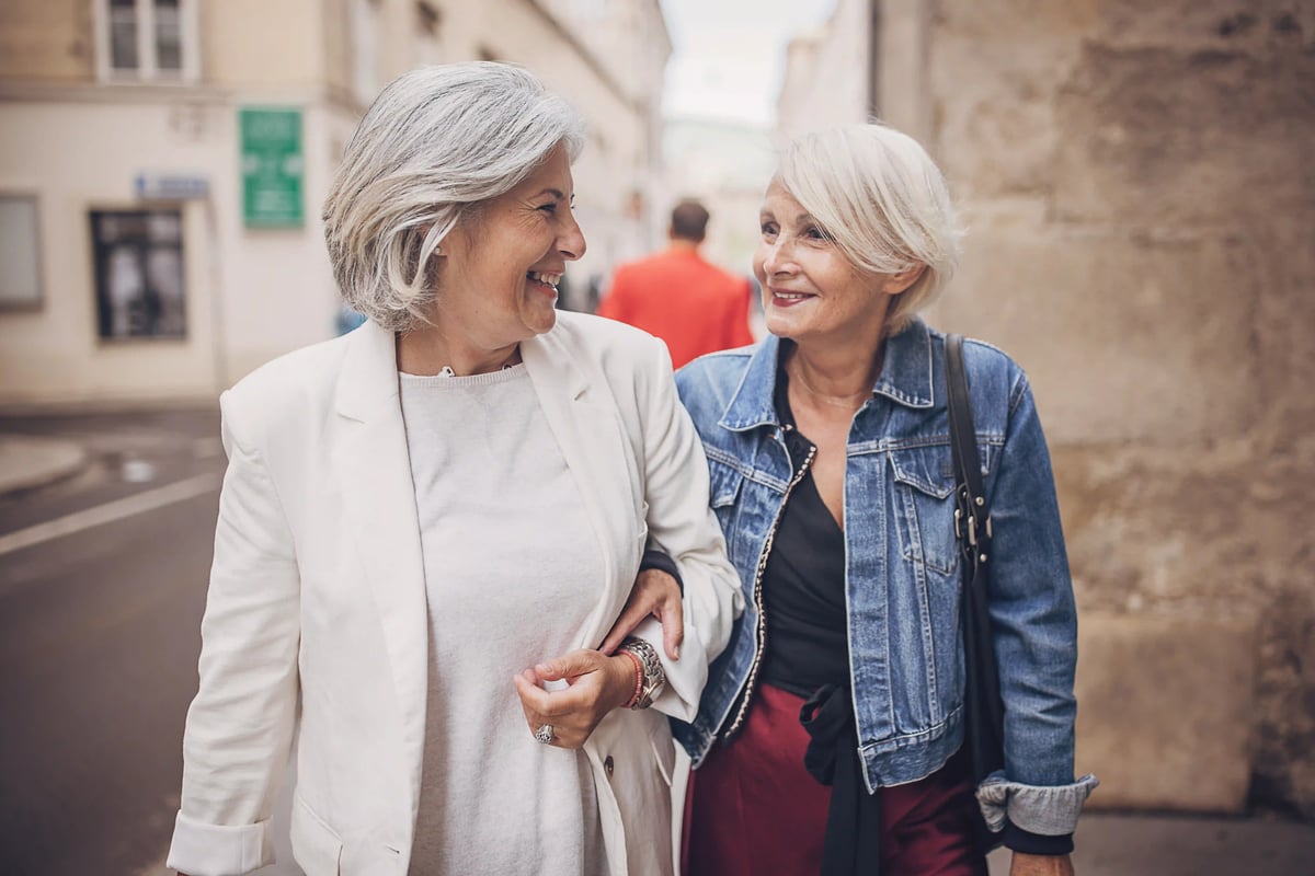 Deux femmes âgées marchent bras dessus bras dessous en souriant dans une rue ancienne étroite