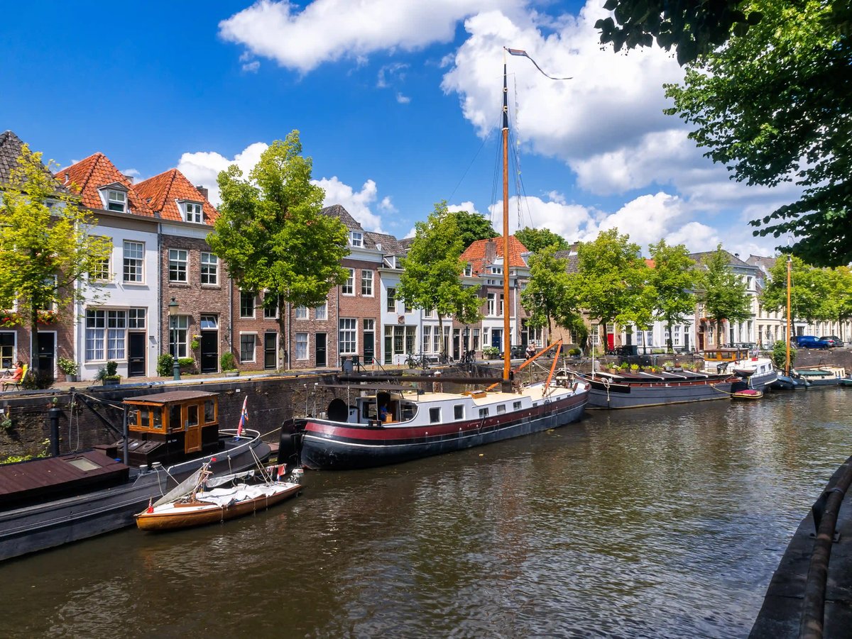 Maisons historiques le long dun canal avec bateaux, bordées darbres sous un ciel bleu