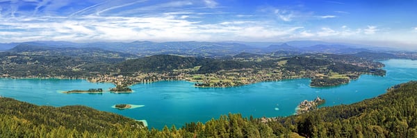 Panoramablick auf den Wörthersee, bewaldeten Ufern und Dörfern unter hellem Himmel