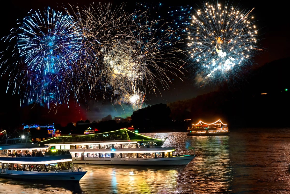Farbenprächtiges Feuerwerk erleuchtet den nächtlichen Rhein mit beleuchteten Schiffen und Uferlichtern