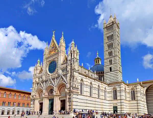 Dom von Siena mit reich verzierter Fassade und gestreiftem Glockenturm; Menschenmenge auf dem Platz bei sonnigem Himmel.