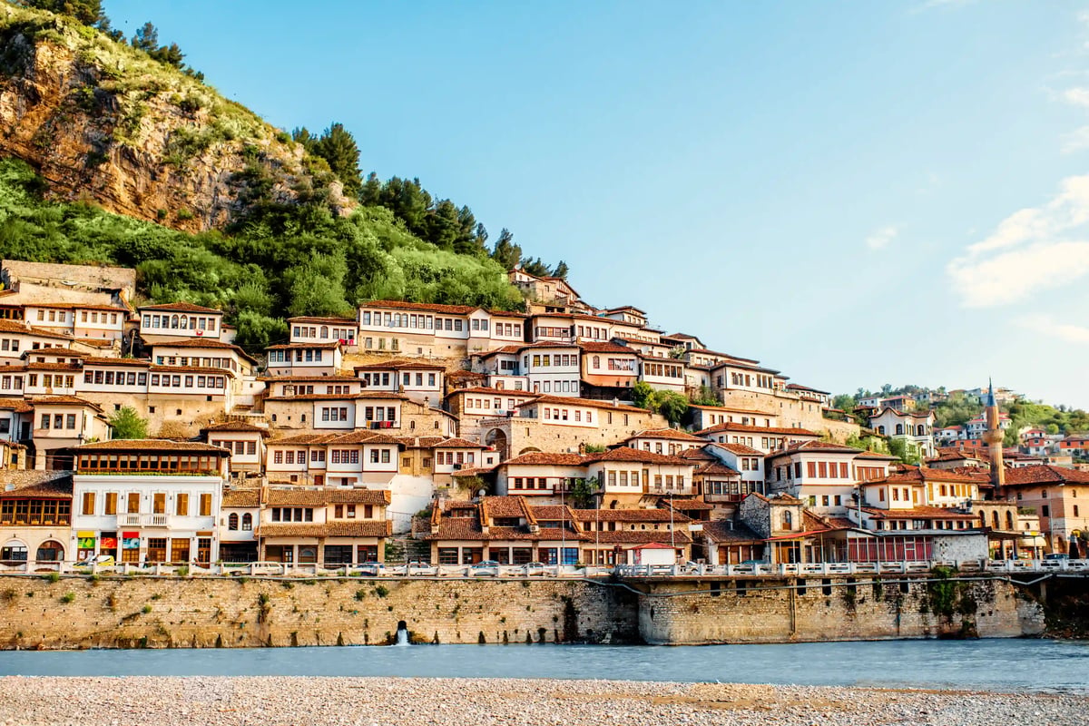 Vue de Berat avec des maisons claires en terrasses sur la colline au-dessus de la rivière, colline verdoyante et ciel bleu