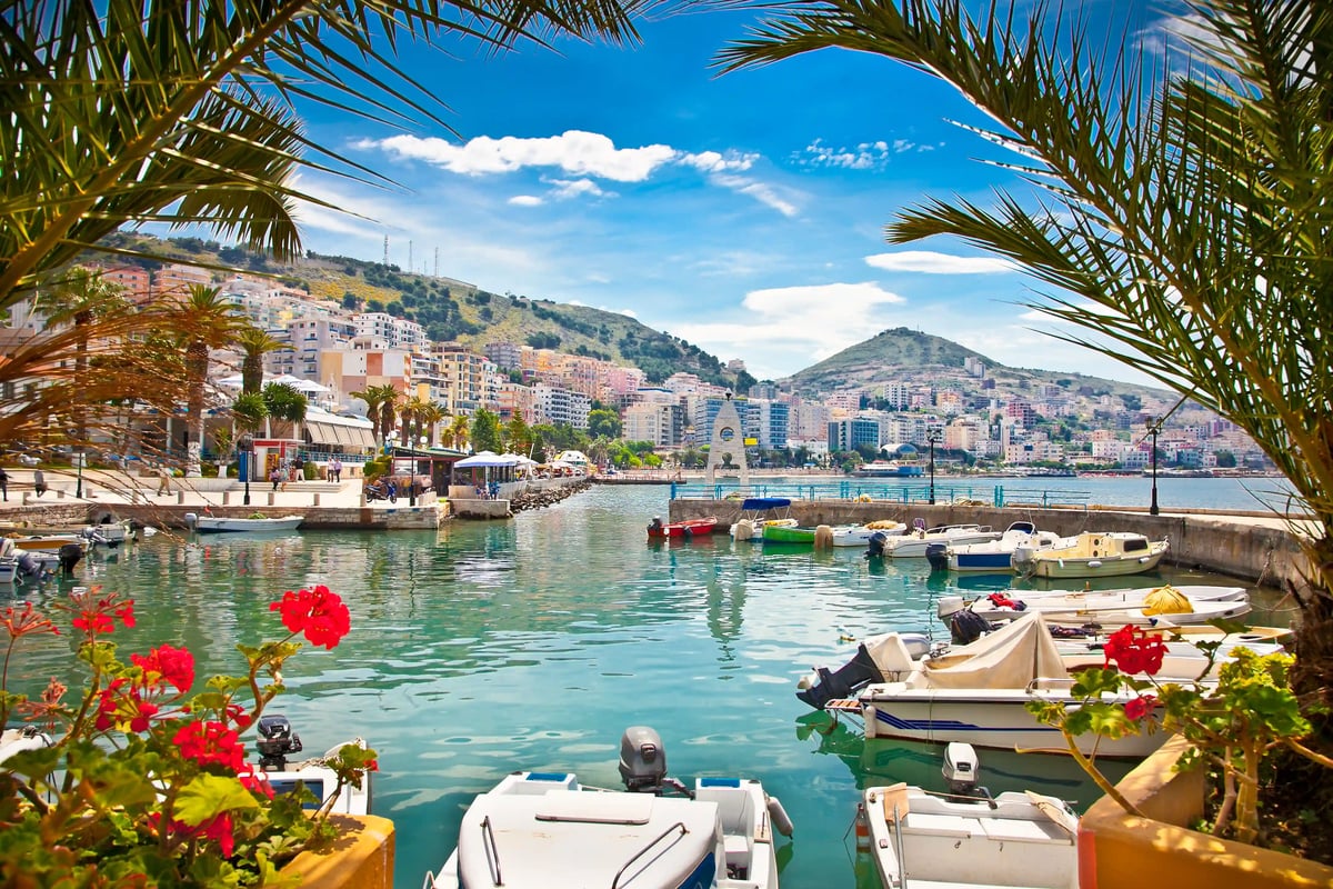 Hafen von Saranda mit kleinen Booten, türkisfarbenem Wasser und Stadt im Hintergrund.