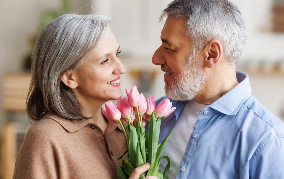 Couple âgé souriant tenant un bouquet de tulipes roses et se regardant avec tendresse