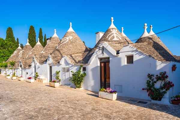 Kopfsteinpflasterstrasse mit weissen Trulli-Häusern und kegelförmigen Dächern in Alberobello, dekoriert mit Pflanzen und Blumen
