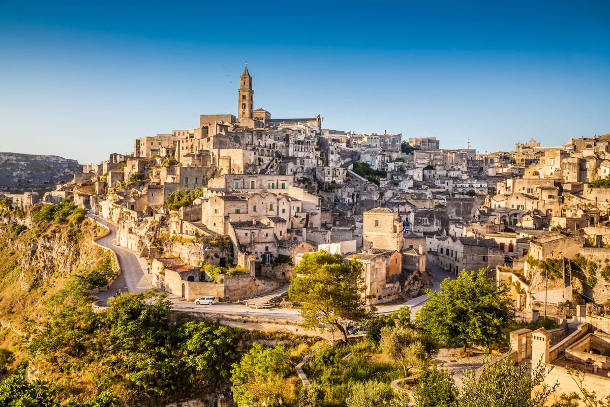 Panoramablick auf die Felsenstadt Matera mit dicht gebauten Steinhaeusern und Kirchen auf einem Huegel ueber einer Schlucht