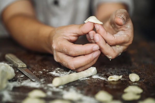 Hände formen frische Orecchiette Pasta aus Teig auf bemehlter Arbeitsfläche während eines Kochkurses