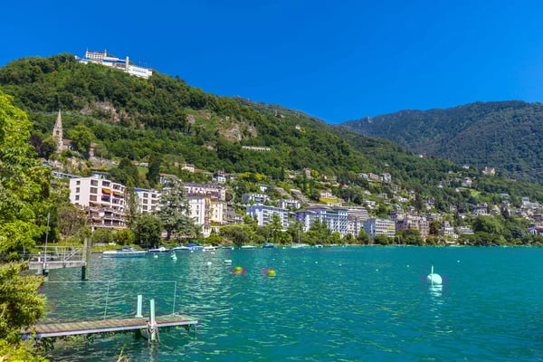 Seepromenade von Montreux mit türkisfarbenem Wasser, Wohnhäusern und bewaldeten Berghängen