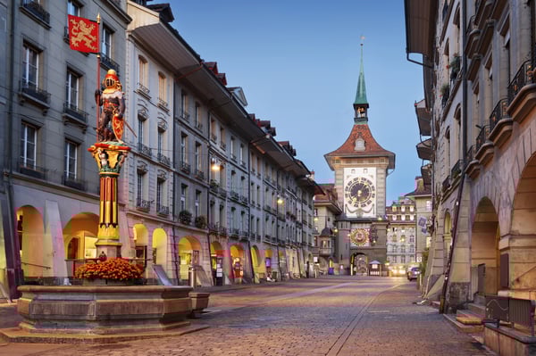 Altstadt von Bern mit gepflasterter Gasse, Laubengängen und dem Zytglogge Uhrturm im Hintergrund, beleuchtet in den Abendstunden