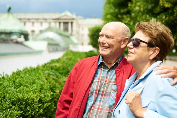 Lächelndes älteres Paar betrachtet gemeinsam eine Sehenswürdigkeit im Grünen vor historischer Architektur