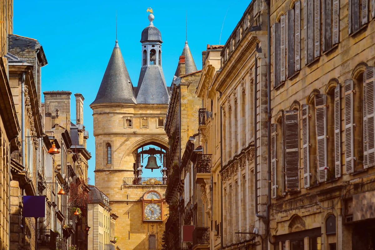 Historische Altstadt von Bordeaux mit steinernen Häusern, schmaler Strasse und markantem Stadttor unter blauem Himmel