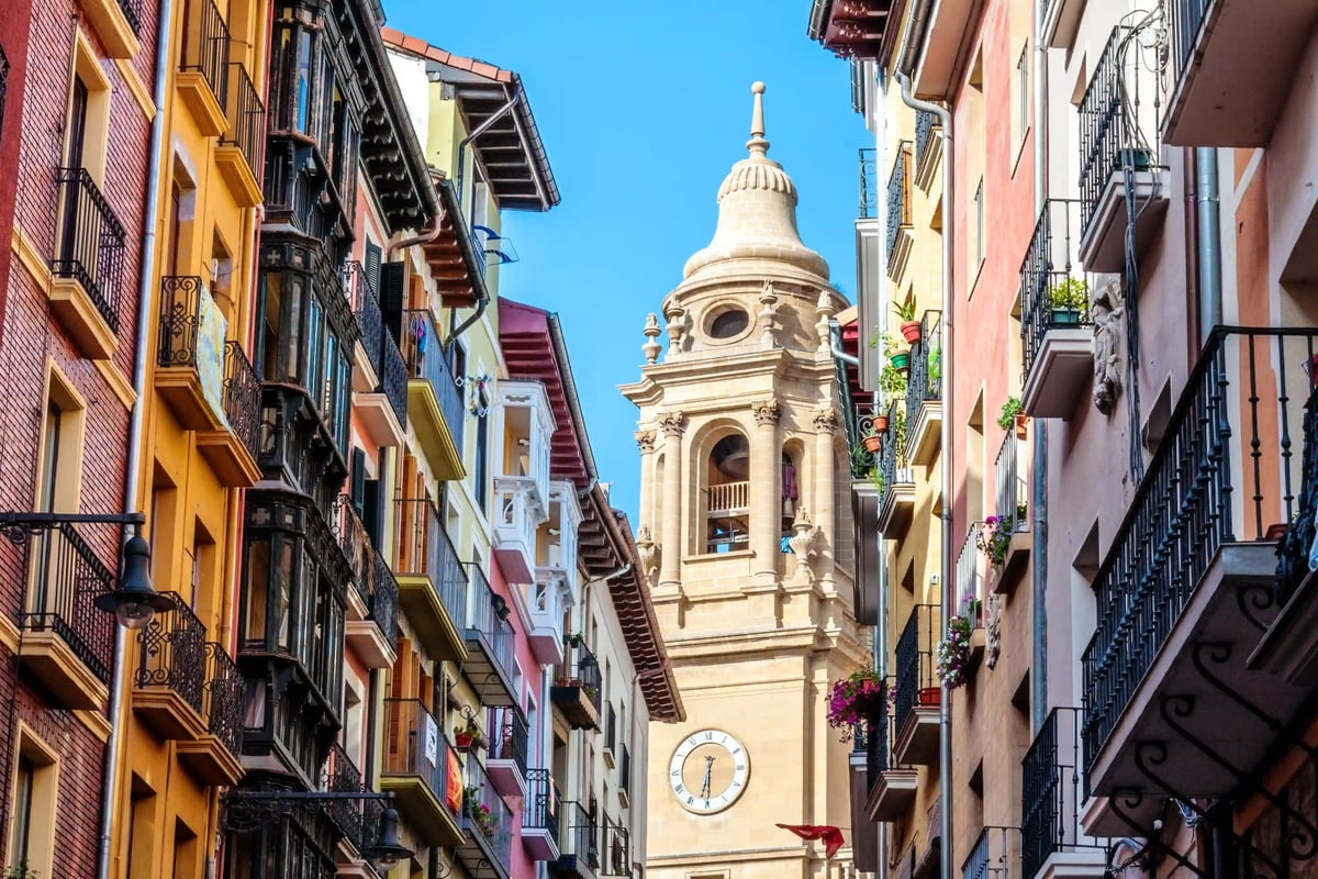 Enge Gasse in Pamplona mit bunten Fassaden, Balkonen und Kirchturm im Hintergrund