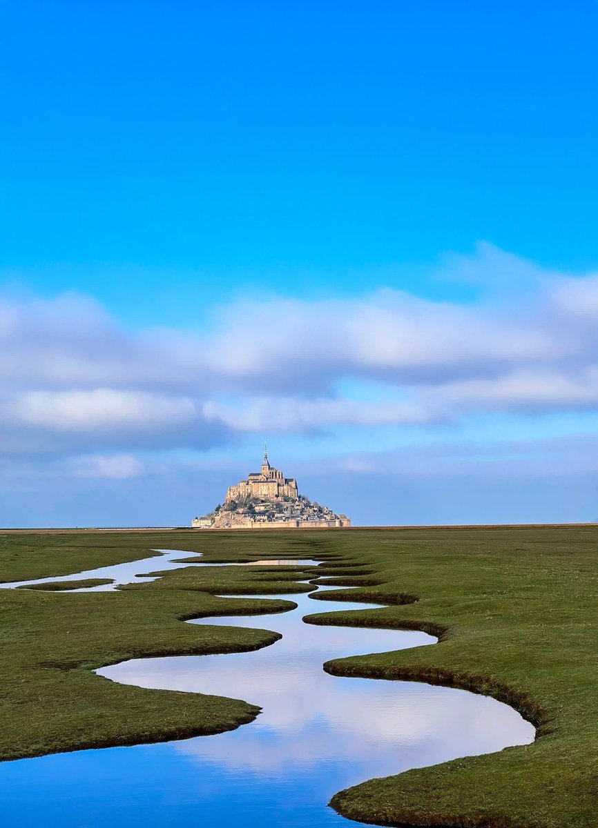 Mont Saint Michel dans un vaste paysage avec un cours d eau sinueux à travers des prés salés sous un ciel bleu
