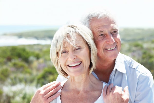 Lächelndes älteres Paar steht eng beieinander in grüner Landschaft und blickt entspannt in die Ferne