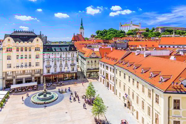 Blick über den Hauptplatz von Bratislava mit historischen Gebäuden, Brunnen und der Burg Bratislava auf einem Hügel im Hintergrund