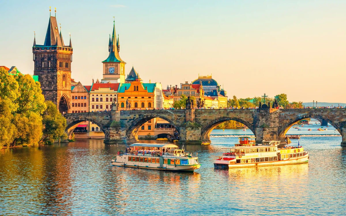 Karlsbruecke in Prag mit historischen Tuermelementen und Ausflugsbooten auf der Moldau