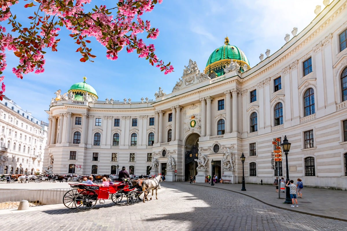 Hofburg in Wien mit weisser Barockfassade, grünen Kuppeln und Pferdekutschen auf dem Platz